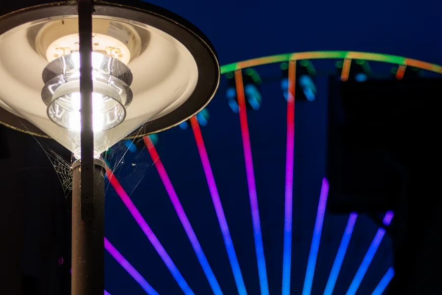 Bunte Lichtstreben eines Riesenrads hinter einer Straßenlaterne