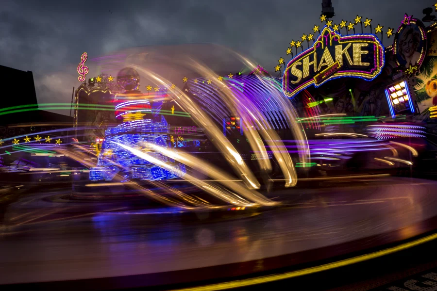 Goldene Lichtspuren eines Fahrgeschäfts vor der leuchtenden Aufschrift Shake