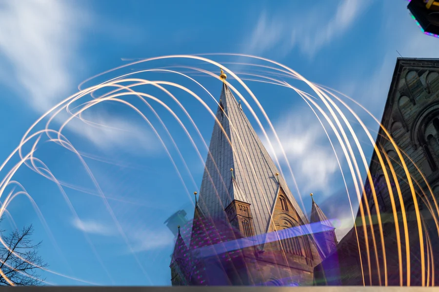 Helle Lichtspuren eines Fahrgeschäfts vor einem Soester Kirchturm