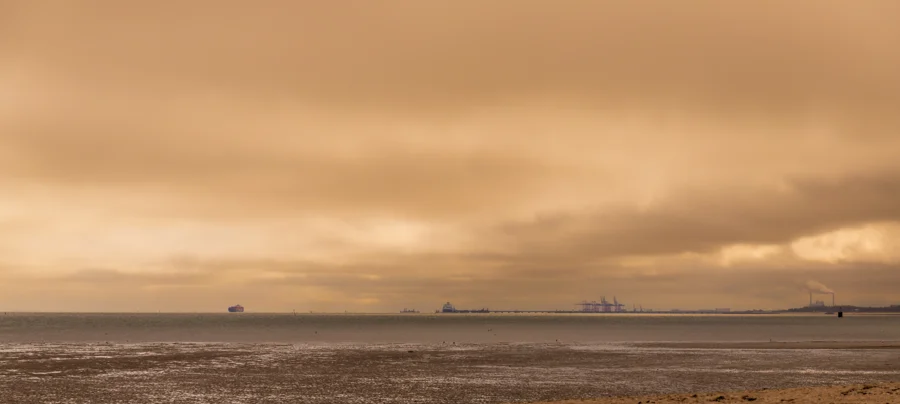 Weite Küstenlandschaft mit warmem Himmel und fernen Schiffen