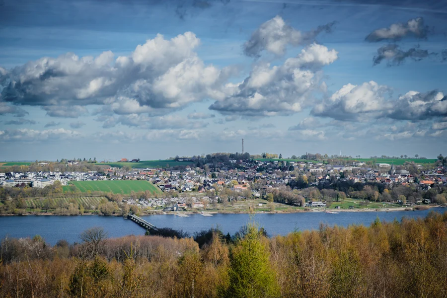 Blick über einen See und eine Brücke auf eine Stadt unter Wolken