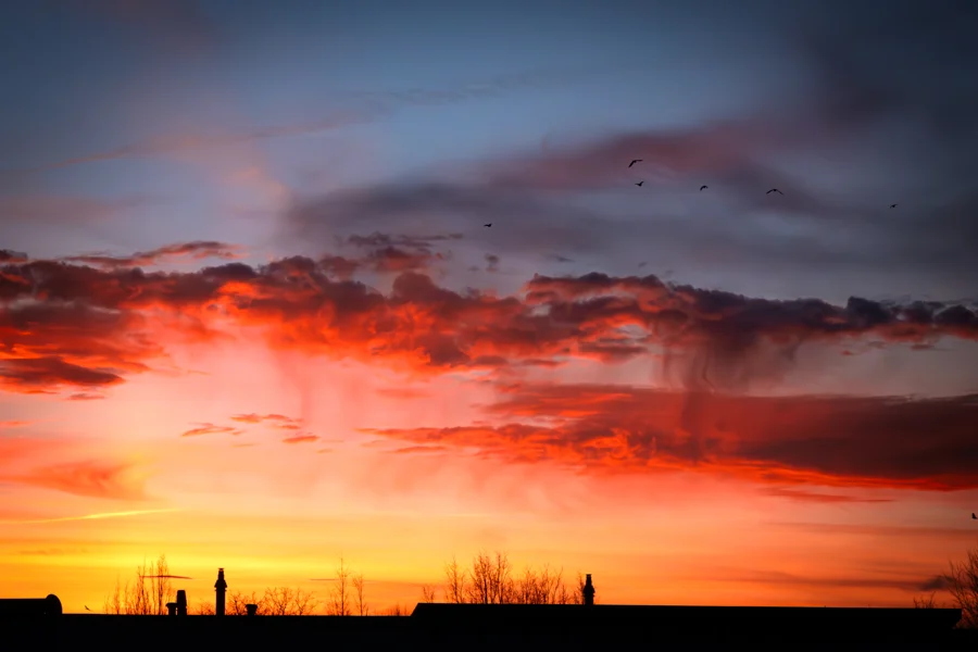 Leuchtend roter und orangefarbener Abendhimmel über einer dunklen Landschaft