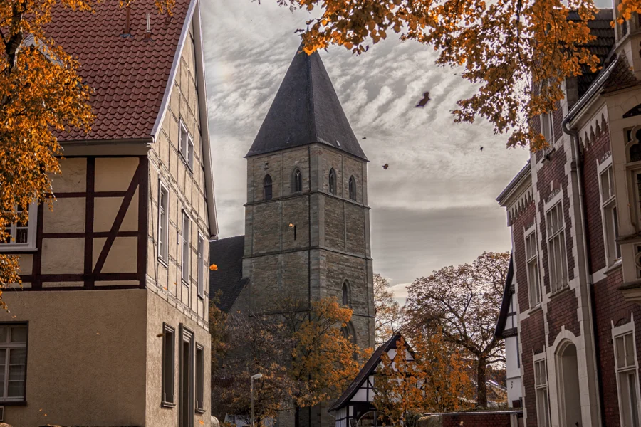 Kirchturm zwischen Fachwerkhäusern und gelben Herbstblättern