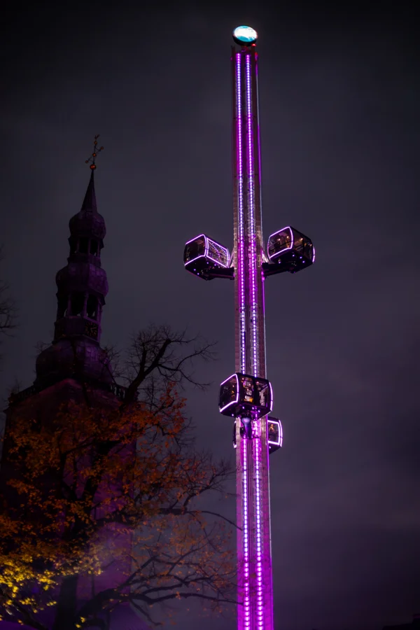 Violett beleuchteter Freifallturm neben Soester Kirchtürmen